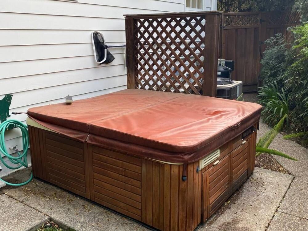 Before: a covered hot tub on a concrete pad beside a house
