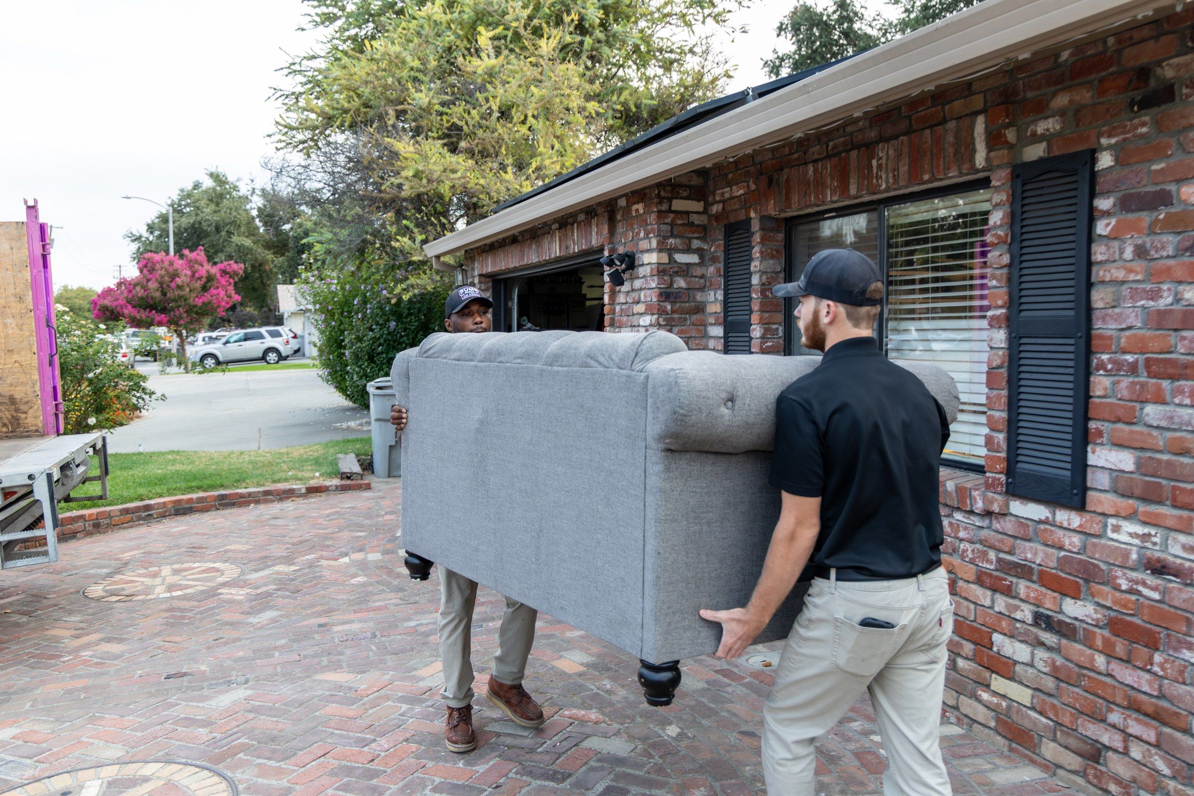 Two Dump Ninja crew members loading a gray sectional couch into the truck at a Woodland home