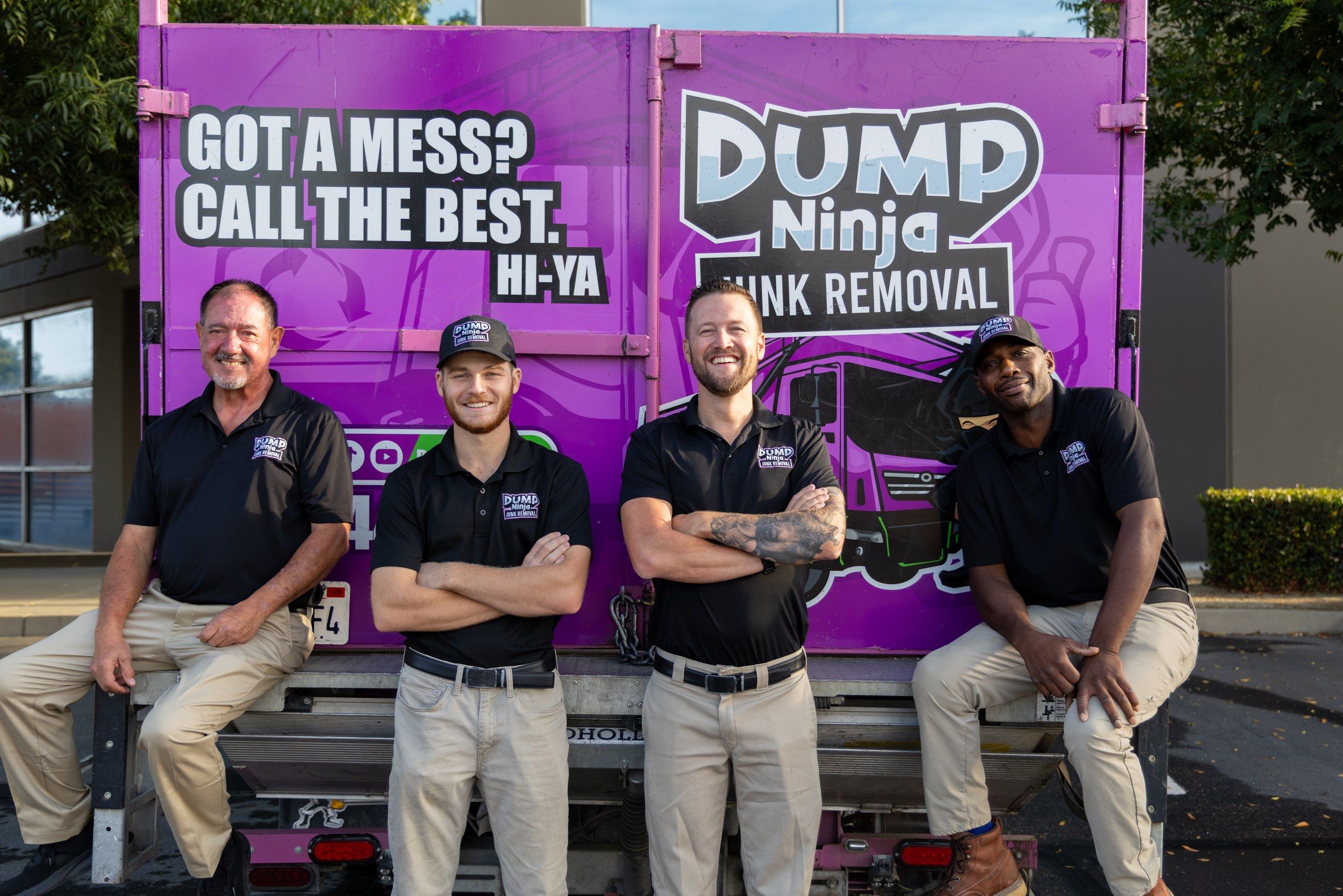 Four Dump Ninja crew members sitting on the tailgate of the magenta junk removal truck in Woodland