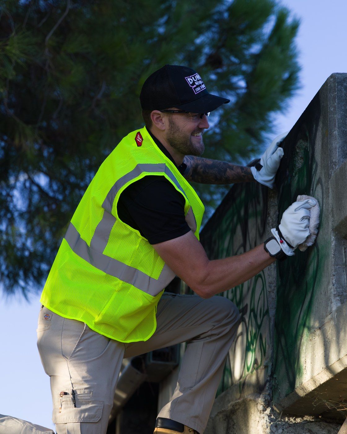 Dump Ninja crew member in a high-visibility vest removing graffiti from a concrete wall